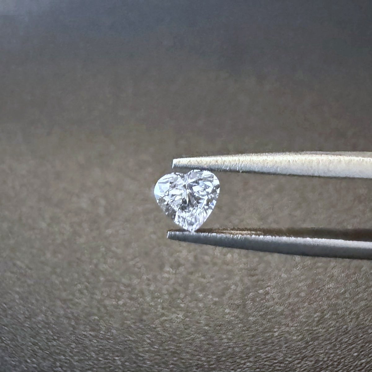 A heart-cut Everlong Gem diamond held in tweezers