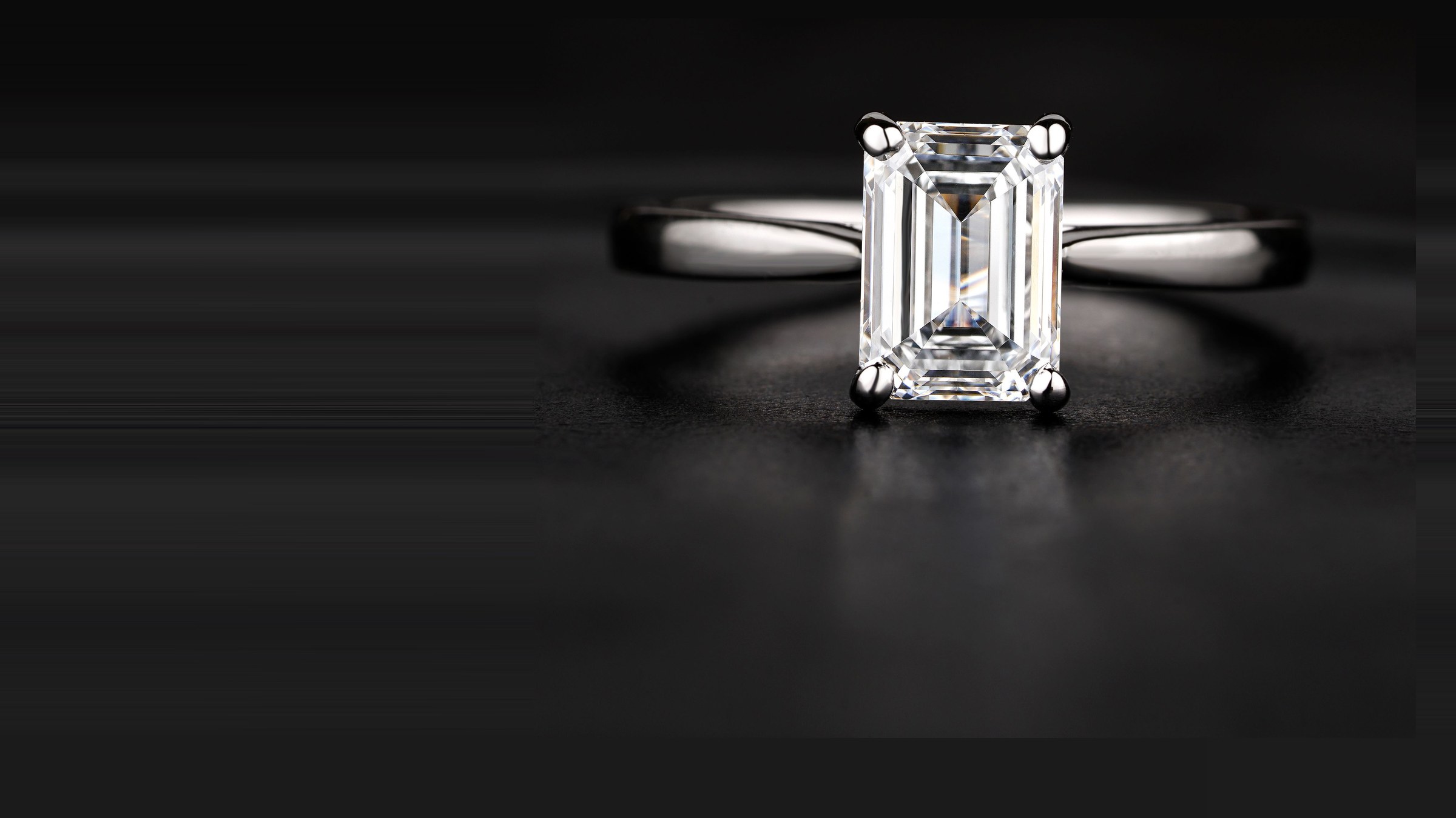 An emerald-cut diamond in a slim platinum solitaire, lit against black